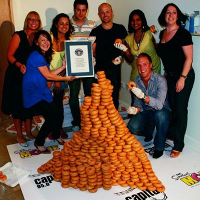 A wobbly pyramid of donuts surrounded by, perhaps undeservedly, proud office workers